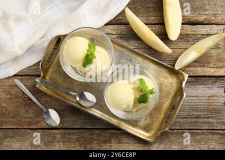 Löffel Melonensorbet mit Minze in Dessertschalen aus Glas, frisches Obst und Löffel auf Holztisch, flach gelegt Stockfoto