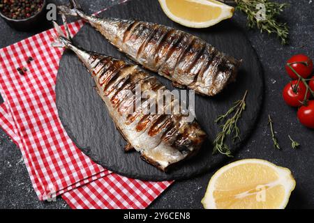 Köstliche gegrillte Makrele, Thymian, Zitrone und Tomaten auf dunkel strukturiertem Tisch Stockfoto