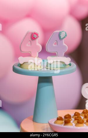 Nahaufnahme von zwei Nummer 4 Geburtstagskeksen mit Pastellfarben auf einem Ständer, mit einem unscharfen rosa Hintergrund, perfekt für ein Kindergeburtstag Thema. Stockfoto