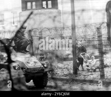29. NOVEMBER 1963 DURCH DEN STACHELDRAHT DER BERLINER MAUER IST EINE FRAU MIT EINEM BABY IM KINDERWAGEN UNTER DEN AUGEN EINES OSTDEUTSCHEN PANZERWAGENS ZU SEHEN, DER TEIL EINES TEAMS IST, DAS MIETER AUS EINEM WOHNBLOCK IN DER SEBASTIAN STRASSE, NAHE DEM GRENZÜBERGANG HEINRICH-HEINE-STRASSE, VERTREIBT. BERLIN, DEUTSCHLAND. Stockfoto