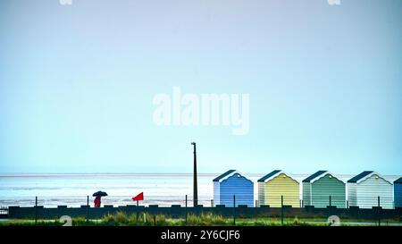 Eine Einzelfigur unter dem Sonnenschirm und eine Reihe farbenfroher Strandhütten, St. Annes, UK Stockfoto