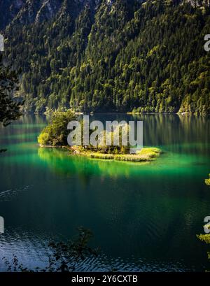 Eine kleine Insel mitten in einem See mit Bäumen umgeben. Das Wasser ist ruhig und klar und spiegelt die Bäume und den Himmel wider. Die Szene ist friedlich Stockfoto