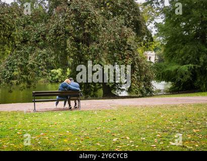 Mann und Frau sitzen auf einer Parkbank mit Blick auf einen See, mit freiem Platz rechts und unten. Stockfoto