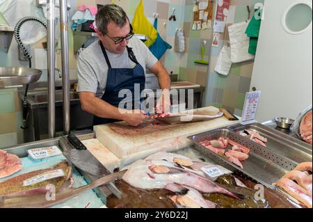 Sesimbra, Portugal - 10. September 2024 : Ein geschickter Fischhändler reinigt und bereitet verschiedene Meeresfrüchte an einem belebten Marktstand zu. Stockfoto