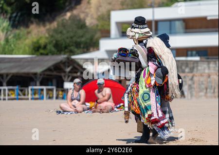 Sesimbra, Portugal - 10. September 2024: Händler verkauft an einem sonnigen Tag handgefertigte Artikel an einem Strand, an dem Touristen sich in der Nähe entspannen Stockfoto