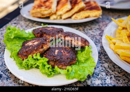 Gegrilltes Burgerschnitzel mit Salatblättern Runde Bällchen mit trockenen Fleischbällchen und Pommes frites. Gebratener Schnitzel-Burger mit Salat auf einem Teller. Hausgemachte Ko Stockfoto