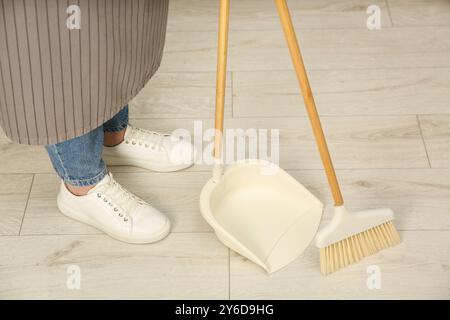 Frau mit Besen und Kehrpfanne, die den Boden drinnen putzt, Nahaufnahme Stockfoto