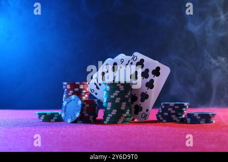 Pokerchips und Spielkarten auf rosa Tisch Stockfoto