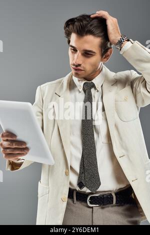 Ein hübscher junger Mann in eleganter formeller Kleidung interagiert mit einem Tablet in einem Studio-Ambiente. Stockfoto