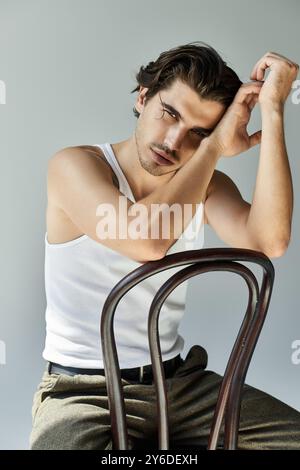 Ein junger Mann mit einem künstlerischen Tattoo lehnt sich nachdenklich an einen Stuhl und zeigt sein entspanntes, aber selbstbewusstes Verhalten. Stockfoto