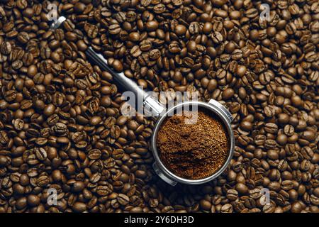 Portafilter mit frisch gemahlenem Kaffee auf der Oberfläche frisch gerösteter Bohnen, Blick von oben. Stockfoto