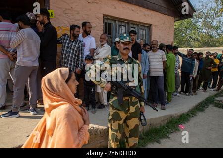 Indischer paramilitärischer Soldat ist wachsam, während die kaschmirischen Wähler in der zweiten Phase der Parlamentswahlen in Budgam, südwestlich von Srinagar, in einer Warteschlange warten, um ihre Stimmzettel vor dem Wahlhaus abzugeben. Dies sind die ersten Kommunalwahlen seit einem Jahrzehnt und die ersten, seit Neu-Delhi 2019 den halbautonomen Status der Region widerrief und sie unter direkte Herrschaft stellte. Fast neun Millionen Menschen sind registriert, um in der umstrittenen Region zu wählen, die traditionell für Boykotte aus Protest gegen die indische Herrschaft bekannt ist. Stockfoto