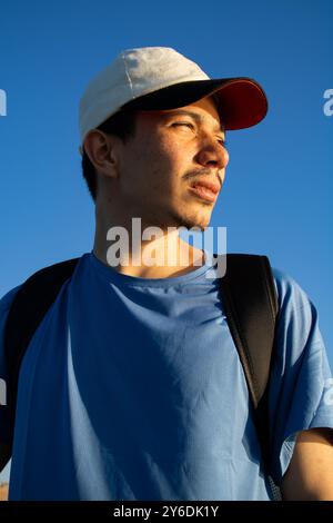 Der Mann bekommt morgens Sonne auf sein Gesicht mit blauem Himmel im Hintergrund und trägt eine Mütze und ein blaues Sporthemd Stockfoto