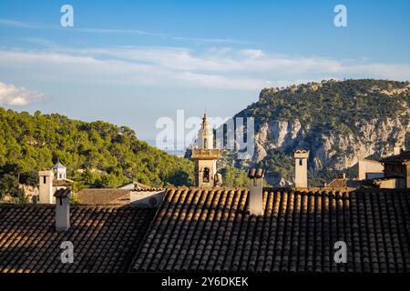 Blick über die Dächer einer kleinen Stadt, wo wir ihre Strukturen sehen, wie die Kirche und kleine Häuser, im Hintergrund die Berge voller Bäume Stockfoto