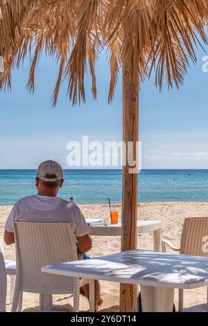 Ein Mann sitzt in einer Strandbar am Strand von Su Giudeu, Italien, bei Bier und Spritz-Cocktail Stockfoto