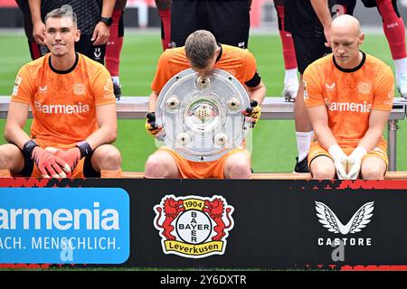 Leverkusen, Deutschland. September 2024. Leverkusener Torhüter Lukas Hradecky (M) schaut sich die Meisterschafttrophäe während der Fotosession der Bundesliga-Fußballmannschaft Bayer 04 Leverkusen an. Quelle: Federico Gambarini/dpa/Alamy Live News Stockfoto