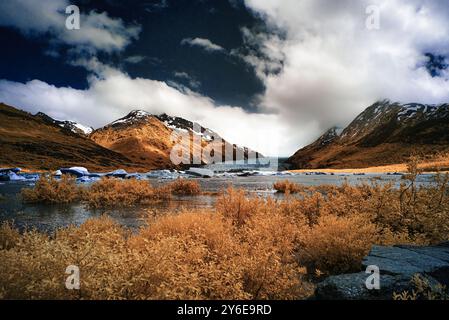 Eine atemberaubende Landschaft mit einem Fluss, der durch ein Tal fließt, mit schneebedeckten Bergen und dramatischen Wolken im Hintergrund. Stockfoto