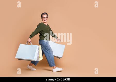 Foto der schönen fröhlichen netten Frau tragen khakifarbene Kleidung tragen Tasche leeren Raum isoliert auf beigefarbenem Hintergrund Stockfoto