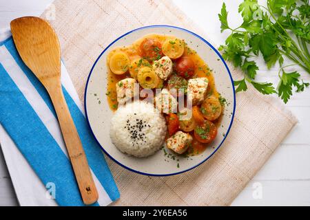 Weißfischeintopf mit Lauch und Kirschtomaten, serviert mit Reis. Tisch mit Draufsicht und Dekoration. Stockfoto