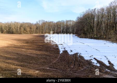 Schmelzender Schnee auf einem gepflügten Feld im Frühjahr. Fruchtbarer schwarzer Boden Stockfoto