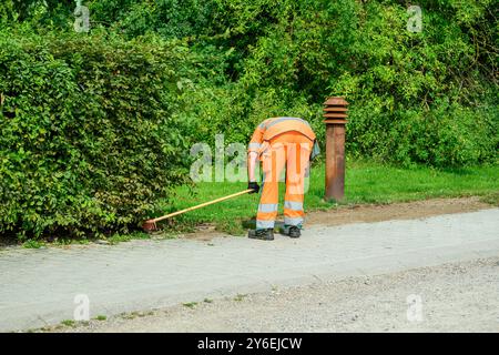 Ein Arbeiter in Sicherheitsausrüstung beugt sich nach unten, um sich in der Nähe eines Hydranten mit einem weißen Fahrzeug auf einem von Bäumen gesäumten Weg in hellem Sonnenlicht zu versorgen Stockfoto