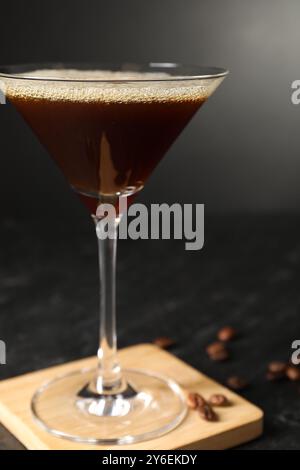 Glas mit köstlichem Espresso Martini und Kaffeebohnen auf dunklem Tisch, Nahaufnahme Stockfoto