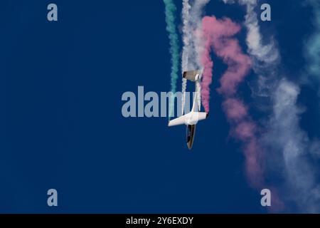 Ein Kunstflieger, der einen Stunt mit farbenfrohen Rauchpfaden vor einem klaren blauen Himmel durchführt. Stockfoto