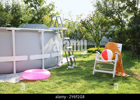 Oberirdischer Swimmingpool, Klappstuhl, Handtuch, aufblasbarer Ring und Ball im Hinterhof Stockfoto