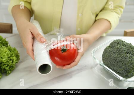 Frau, die Plastikfolie über Tomaten auf der Arbeitsplatte in der Küche legt, Nahaufnahme Stockfoto