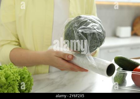 Frau, die Plastikfolie über Brokkoli auf der Arbeitsplatte in der Küche legt, Nahaufnahme Stockfoto