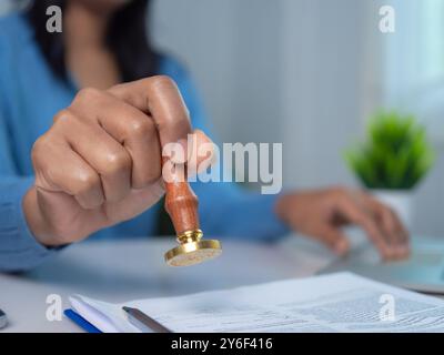 Geschäftsfrau stempelt Handstempel mit genehmigtem Stempel auf dem genehmigten Dokument am Schreibtisch, validiert und verwaltet Geschäftsdokumente und Vereinbarungen, Genehmigungen Stockfoto