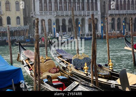 Gondeln, die auf dem Canal Grande in Venedig vertäut sind, während eine einzige Gondel Touristen für eine Fahrt im Hintergrund mitnimmt. Stockfoto