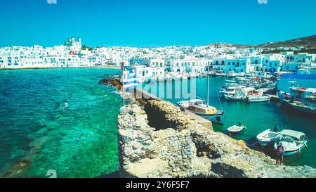 Farbfoto der griechischen Nationalflagge, die auf den Ruinen der venezianischen Burg winkt, mit Blick auf eine Stadt Naoussa als Hintergrund, Paros Insel, Griechenland Stockfoto