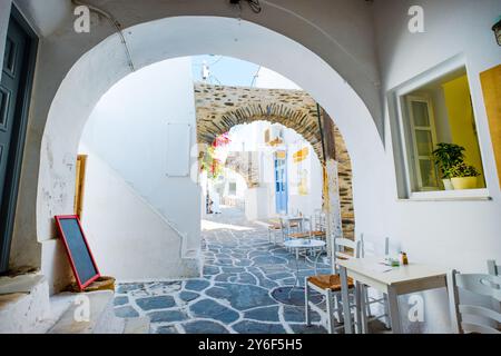 Enge Straße mit Bögen und weißen Häusern. Weiße Tische und Stühle des gemütlichen Straßencafés in Naoussa, Paros, Griechenland Stockfoto