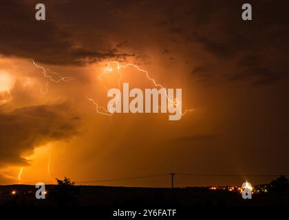 Ein dramatischer Nachthimmel, beleuchtet durch Blitze über einer fernen Stadt mit Lichtern am Horizont. Stockfoto