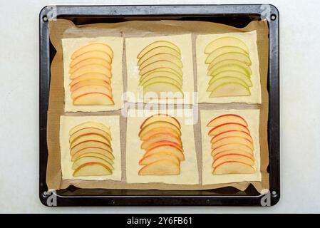 Geschnittene Apfelstücke werden auf Blätterteigplatten auf einem mit Backpapier überzogenen Blech ordentlich angeordnet. Konzept des hausgemachten Backens und Backens Stockfoto