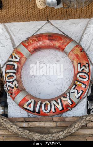 Alter orangener Rettungsring aus Kunststoff mit griechischer Schrift um den Rand, der an der Wand der Taverne in Griechenland als maritimes nautisches Dekor hängt Stockfoto