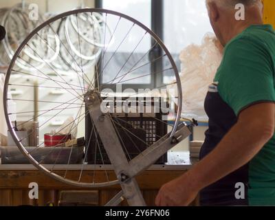 Ein leitender Mechaniker montiert in einer kleinen Fahrradwerkstatt einen Reifen auf ein Rad und zeigt mit Vintage-Werkzeugen Präzision und Qualität Stockfoto