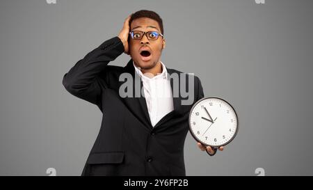 Schockiert afro Kerl holding Wanduhr mit weißem Hintergrund Stockfoto