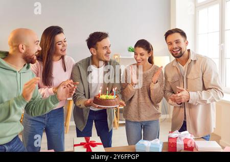 Glücklicher Mann, der Kuchen hält und mit Freunden steht und ihm zu einer Geburtstagsparty gratuliert Stockfoto