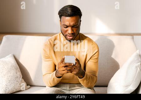 Discontended Mann hält Smaprtphone lesen Nachricht Sitzen auf einem Sofa Indoor Stockfoto
