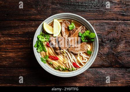 Pho Bo vietnamesische Suppe, Schüssel frische asiatische Suppe mit Reisnudeln, Rindfleisch, Kräutern, Sojasprossen und Chili auf dunklem Holzhintergrund, Blick von oben. Asiatische Küche Stockfoto