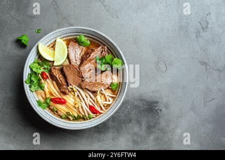 Pho Bo vietnamesische Suppe, Schüssel frische asiatische Suppe mit Reisnudeln, Rindfleisch, Kräutern, Sojasprossen und Chili auf Betonhintergrund, Draufsicht, Kopierraum. De Stockfoto