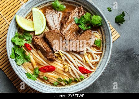 Pho Bo vietnamesische Suppe, Schüssel frische asiatische Suppe mit Reisnudeln, Rindfleisch, Kräutern, Sojasprossen und Chili auf Betonhintergrund, Draufsicht. Asiatische Küche, Stockfoto