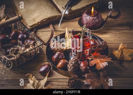 Obsttee für kalte Herbsttage, Kastanien mit Herbstblättern und altes Buch Stockfoto