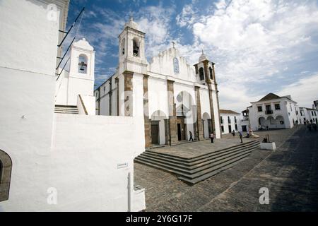 Die befestigte Kirche von Monsaraz steht im Dorf, umgeben von historischer Architektur vor einem blauen Himmel. Stockfoto