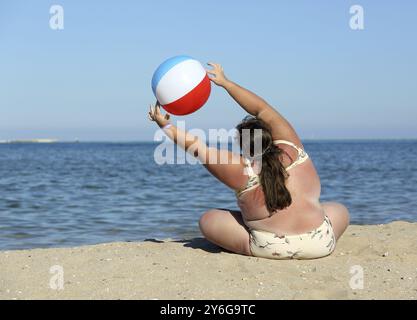 Übergewichtige Frau, die am Strand mit Ball Turnen macht Stockfoto