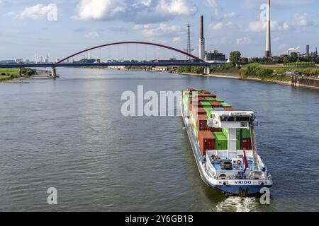 Das mit Containern beladene holländische Frachtschiff Vrido auf dem Rhein bei Duisburg, das hinter der sogenannten Solidaritätsbrücke über den Rhein hinabfährt; Stockfoto