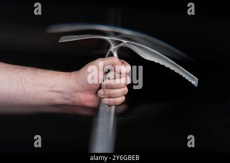 Nahaufnahme der Hand eines Mannes, der eine Eisaxt mit Bewegungseffekt vor schwarzem Hintergrund hält Stockfoto