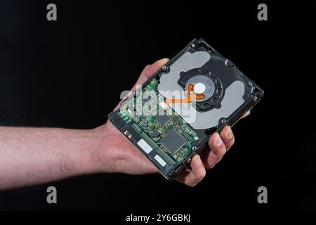 Nahaufnahme der Hand eines Mannes, der eine Computerfestplatte vor schwarzem Hintergrund hält Stockfoto